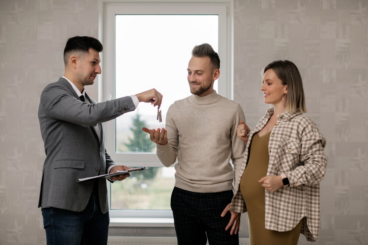 services-03 A pregnant woman and her partner receive house keys from a real estate agent indoors.